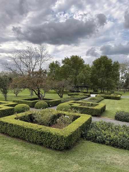 Jardín formal de boj con canteros cuadrados y una pérgola al fondo